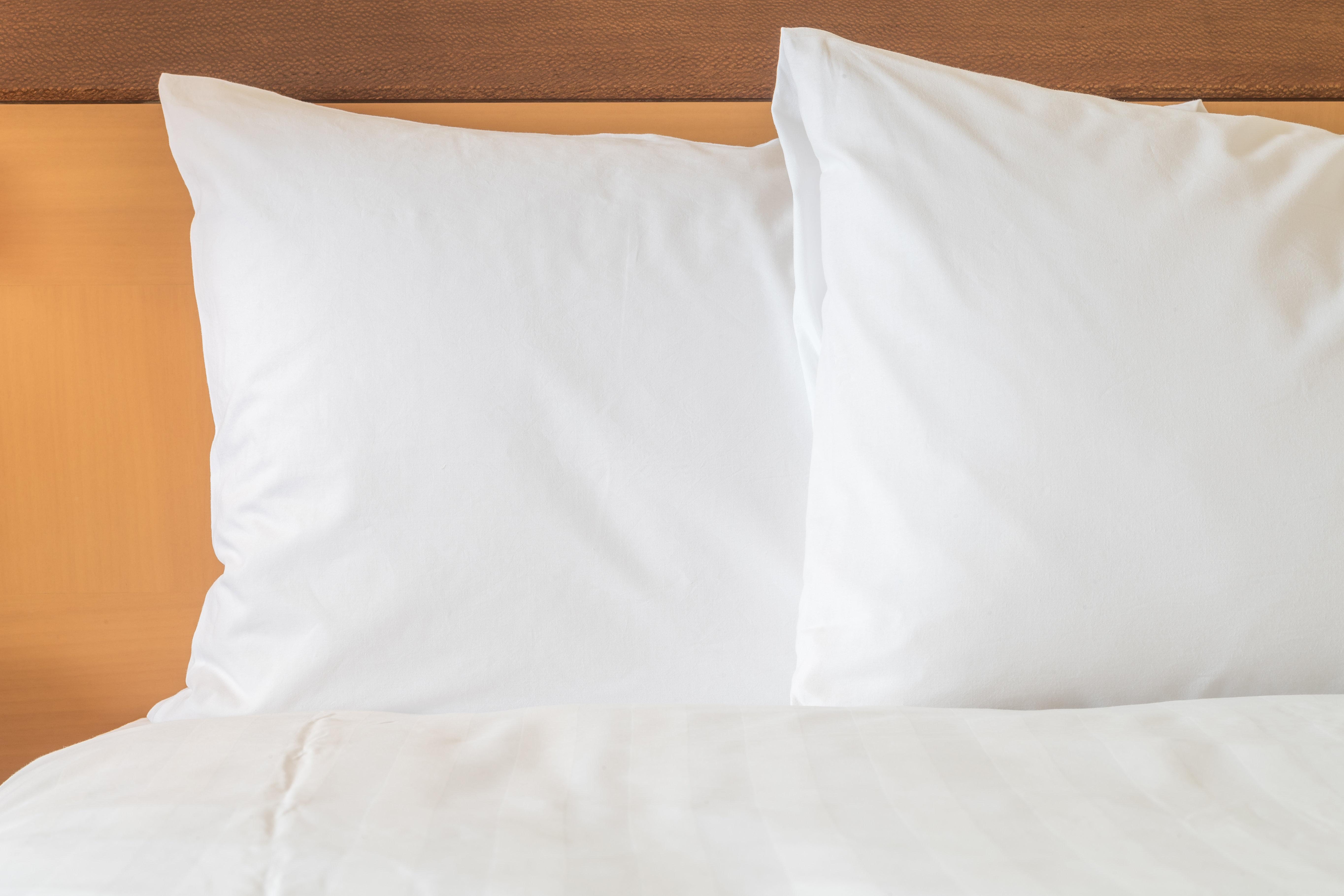 Millennium Hilton Bangkok Hotell Eksteriør bilde The photo shows a close-up of two white pillows on a bed. The pillows are resting against a wooden headboard, and there is a white bedspread visible at the bottom of the image. The overall color scheme is light and neutral, conveying a clean and simp