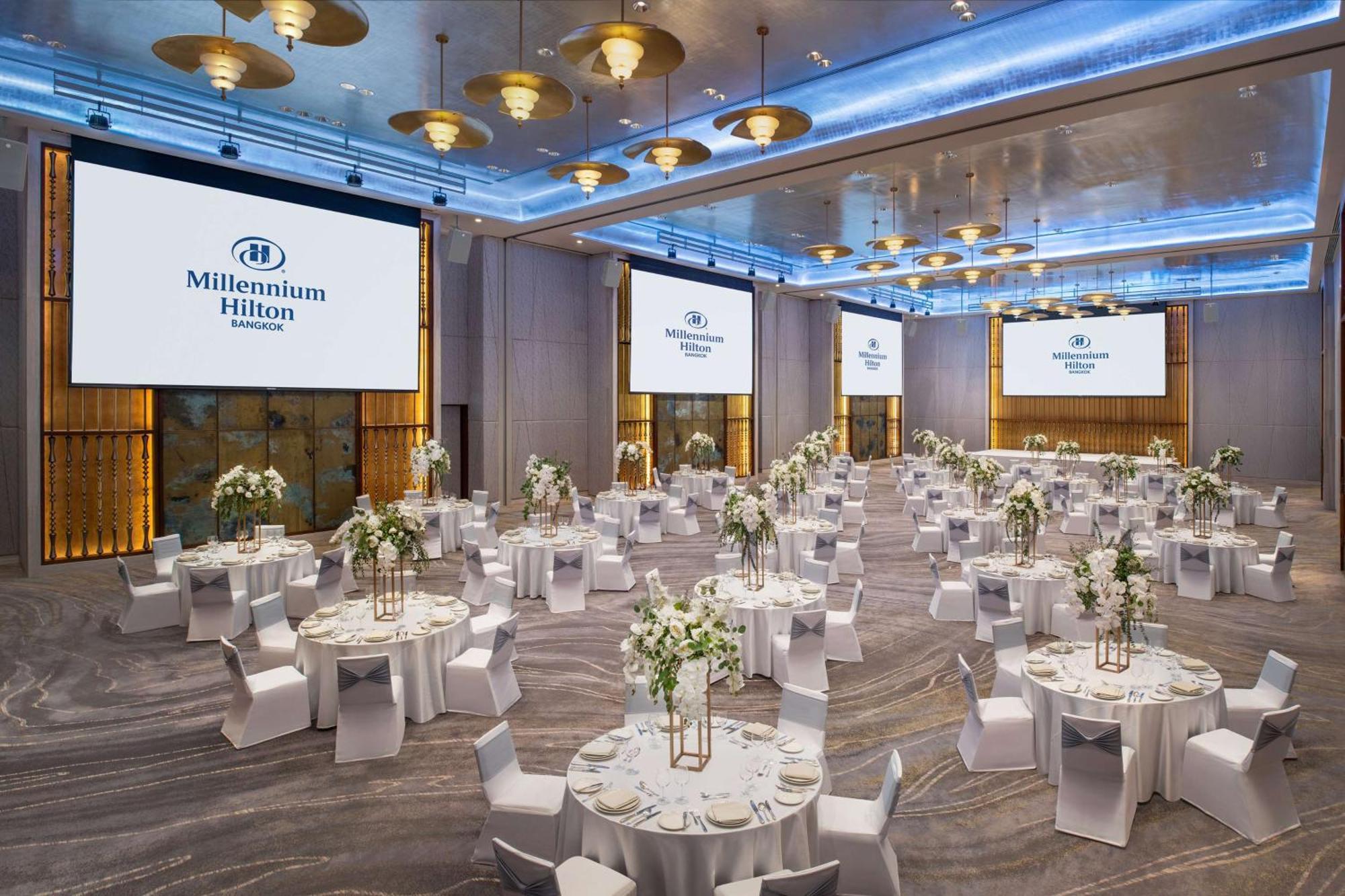 Millennium Hilton Bangkok Hotell Eksteriør bilde The photo shows a large banquet hall set up for an event. The room features multiple round tables covered with white tablecloths, each adorned with floral centerpieces. The chairs are also white, creating a cohesive and elegant look. There are large 